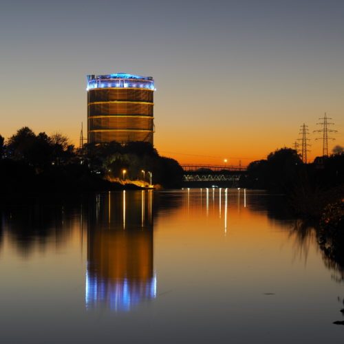 The photo shows the Gasometer Oberhausen and the Rhine-Herne Canal at sunset