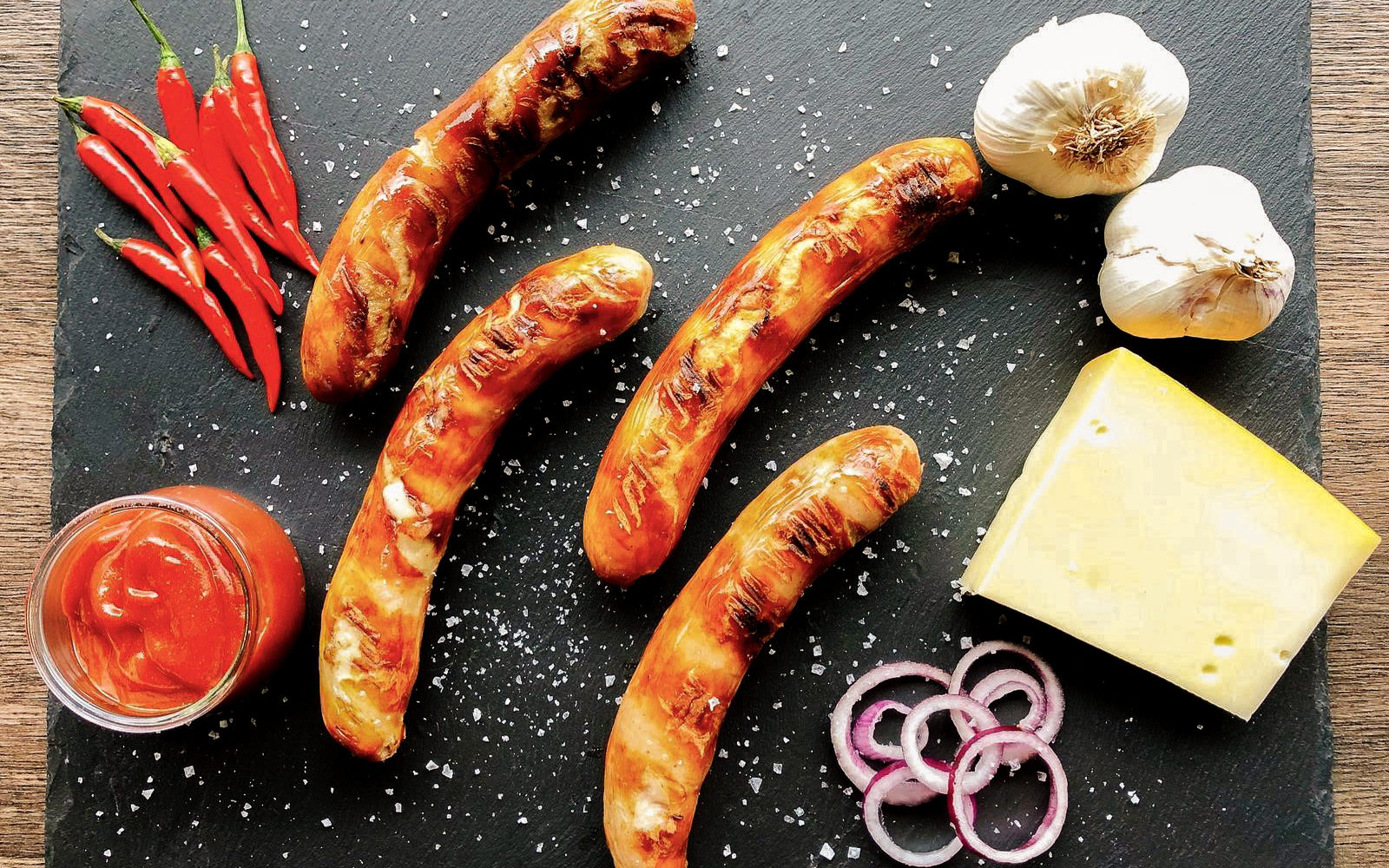 Das Foto zeigt Bratwürste, Knoblach, Chili, Zwiebeln, Käse und Ketchup für eine Ruhrpott Currywurst