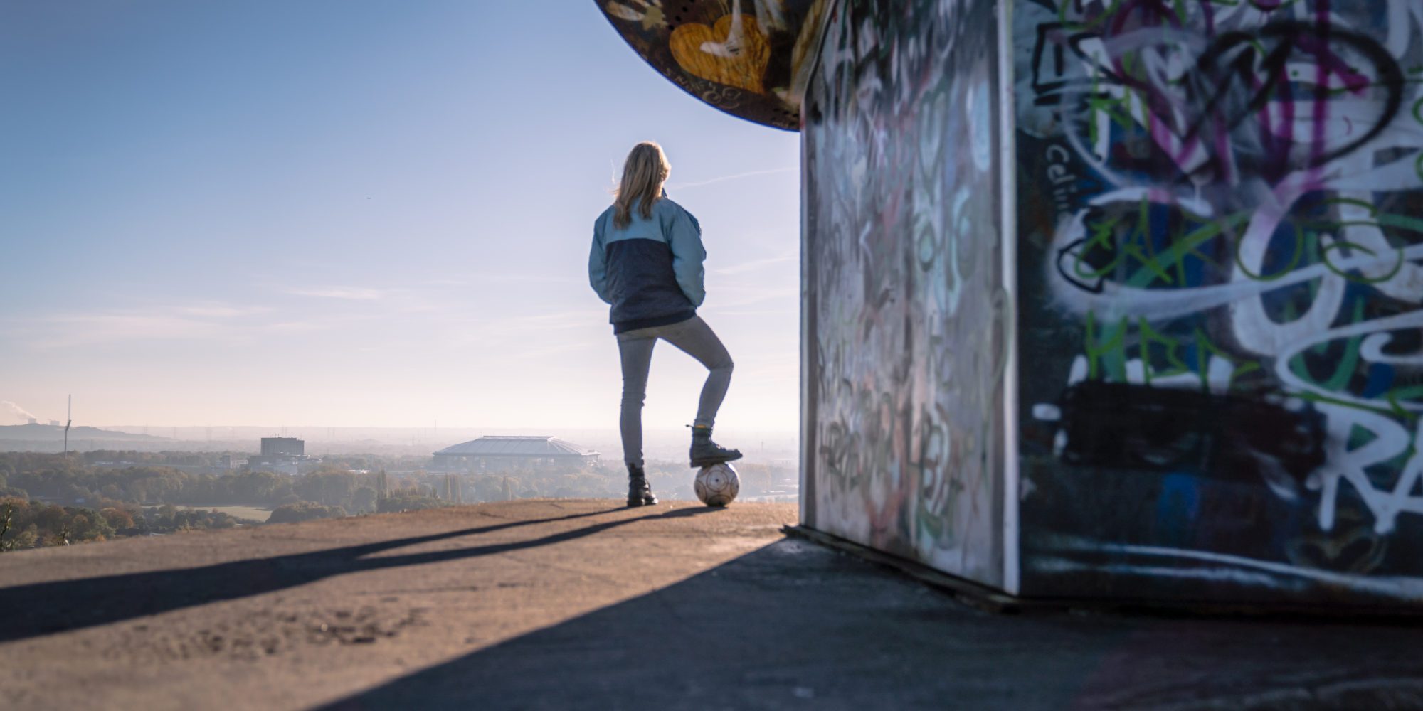 Das Bild zeigt eine Frau auf der Halde Rungenberg in Gelsenkirchen mit Blick zur Arena auf Schalke