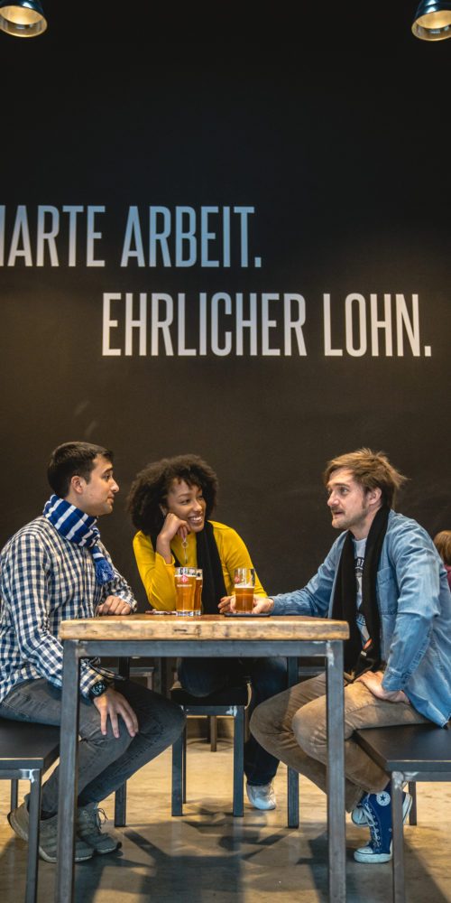 Das Bild zeigt ein paar Menschen in der Stehbierhalle der Bergmann Brauerei in Dortmund