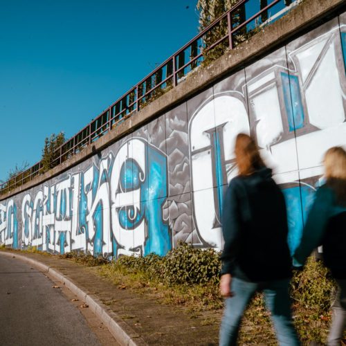 Das Bild zeigt zwei Menschen vor einem Schalke 04 Graffiti