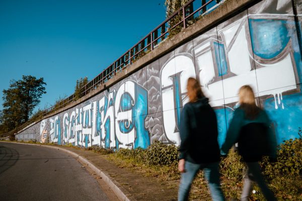 Das Bild zeigt zwei Menschen vor einem Schalke 04 Graffiti