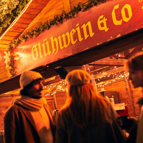 Das Bild zeigt drei Personen vor einem Stand auf dem Weihnachtsmarkt in Dortmund